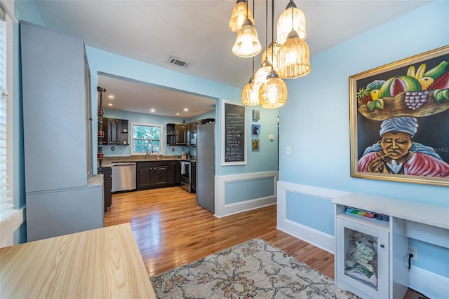 kitchen featuring stainless steel appliances, visible vents, dark brown cabinetry, a sink, and light wood-type flooring