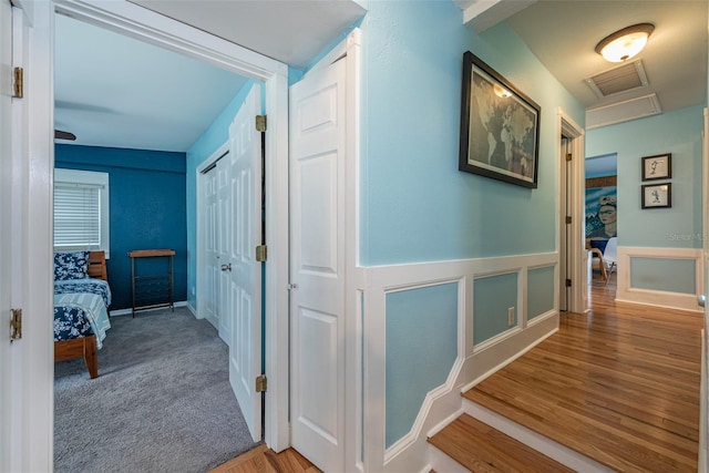 hall with attic access, visible vents, wood finished floors, and wainscoting