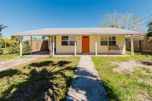 view of front facade featuring covered porch, an attached carport, a front yard, and fence