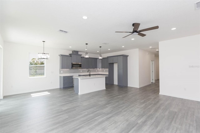 kitchen with gray cabinets, a kitchen island with sink, open floor plan, and stainless steel microwave