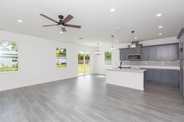 kitchen with open floor plan, stainless steel microwave, wood finished floors, and decorative backsplash