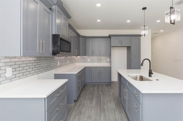 kitchen with a kitchen island with sink, stainless steel microwave, a sink, and gray cabinetry