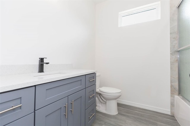 bathroom featuring toilet, wood finished floors, vanity, baseboards, and combined bath / shower with glass door