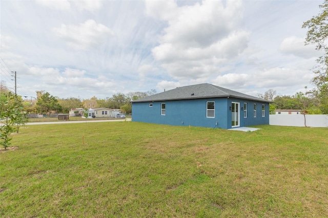 back of house featuring stucco siding, fence, and a yard