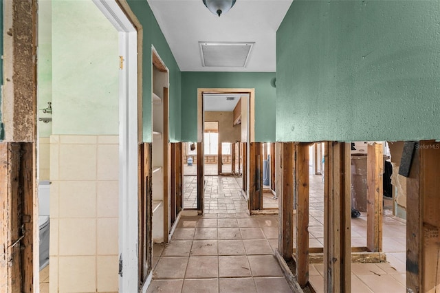 corridor with visible vents, tile patterned floors, attic access, and tile walls