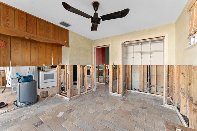 interior space featuring white electric stove, visible vents, a ceiling fan, brown cabinetry, and stone finish floor