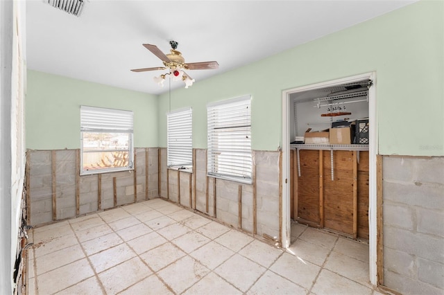 unfurnished room featuring a wainscoted wall, visible vents, plenty of natural light, and ceiling fan