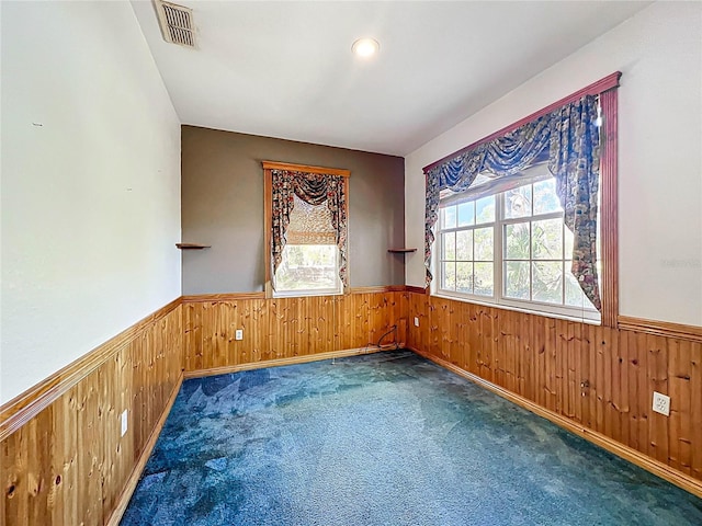 spare room featuring visible vents, wainscoting, a healthy amount of sunlight, and wood walls