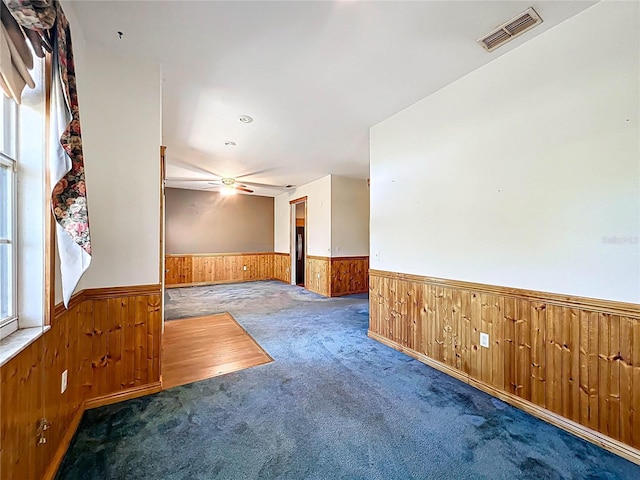 empty room featuring wooden walls, carpet, a wainscoted wall, and visible vents