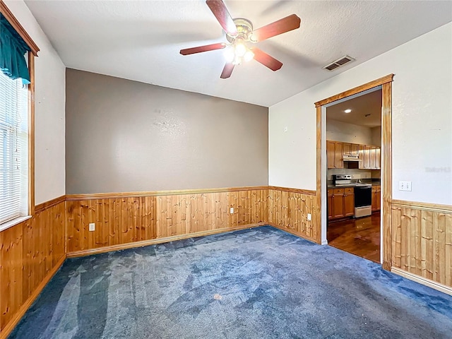 empty room with wooden walls, visible vents, and wainscoting