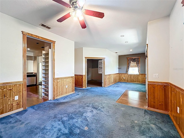 unfurnished room with wooden walls, carpet, wainscoting, and visible vents