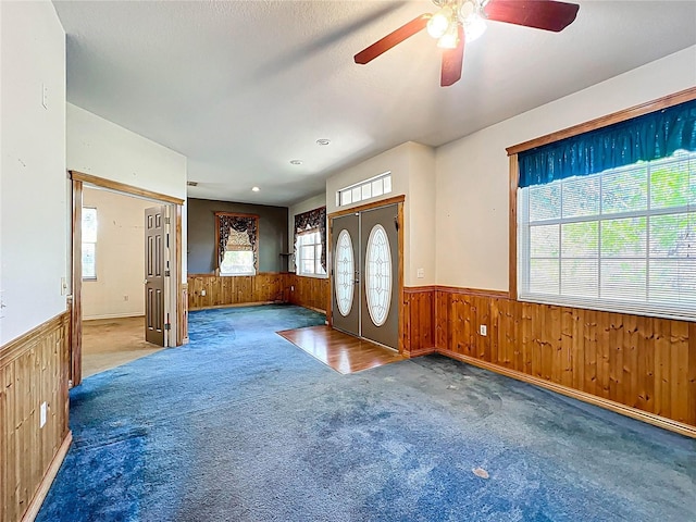 carpeted entryway with a wainscoted wall, a healthy amount of sunlight, and wooden walls