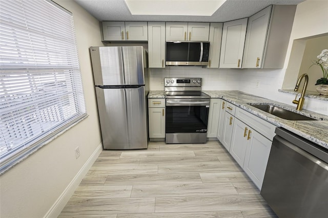 kitchen featuring light stone counters, light wood-style flooring, a sink, appliances with stainless steel finishes, and tasteful backsplash