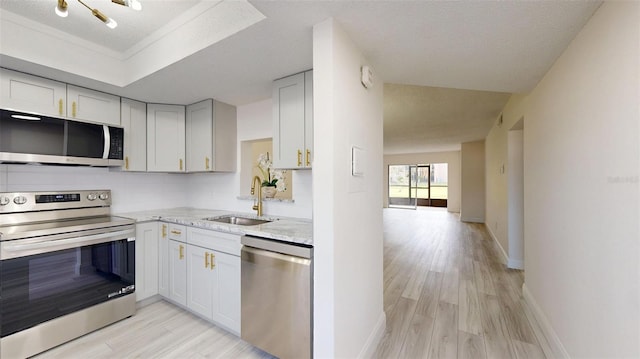 kitchen featuring stainless steel appliances, a sink, baseboards, decorative backsplash, and light wood finished floors