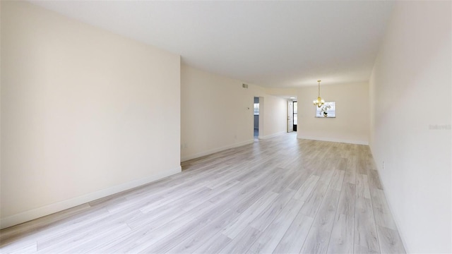 empty room featuring a chandelier, visible vents, light wood-style flooring, and baseboards