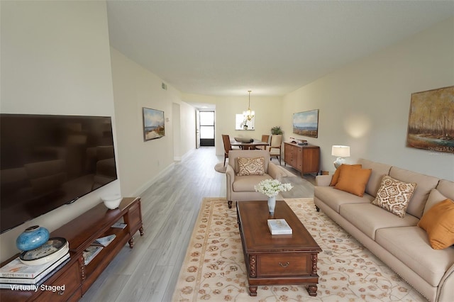 living room featuring light wood-type flooring, visible vents, baseboards, and an inviting chandelier