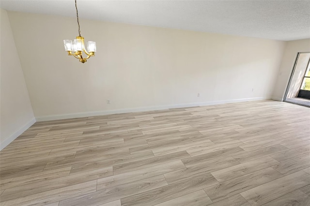 empty room with light wood-type flooring, a notable chandelier, a textured ceiling, and baseboards