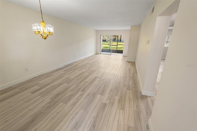 spare room featuring visible vents, a textured ceiling, light wood finished floors, baseboards, and a chandelier