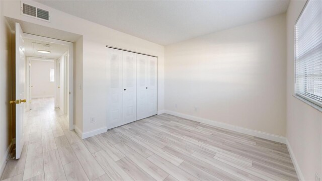 unfurnished bedroom featuring visible vents, baseboards, a closet, and light wood finished floors