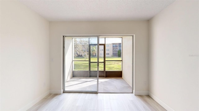 doorway to outside with baseboards, light wood-style floors, and a textured ceiling