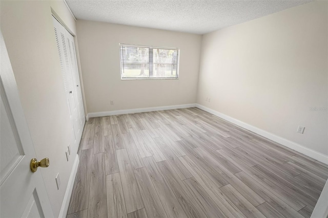 unfurnished bedroom with light wood-style floors, a closet, a textured ceiling, and baseboards