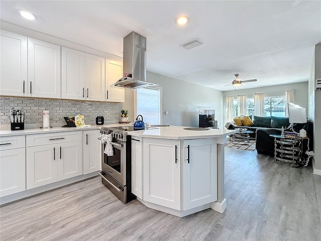 kitchen with stainless steel range with electric stovetop, light countertops, island exhaust hood, and a peninsula