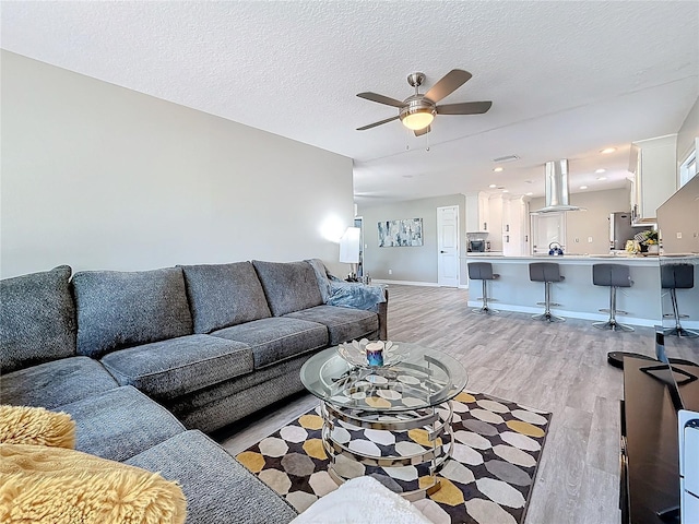 living area featuring a ceiling fan, baseboards, a textured ceiling, and light wood finished floors