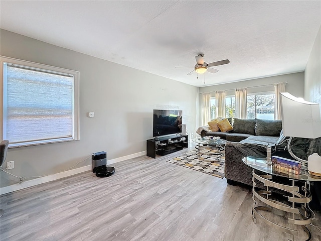 living room with light wood finished floors, ceiling fan, baseboards, and a textured ceiling