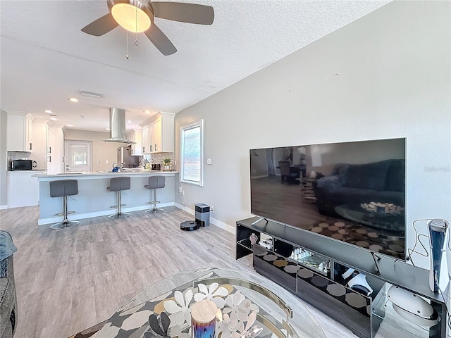 living area featuring baseboards, visible vents, a ceiling fan, a textured ceiling, and light wood-type flooring