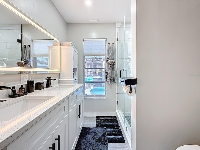 full bathroom featuring a stall shower, a sink, baseboards, and double vanity