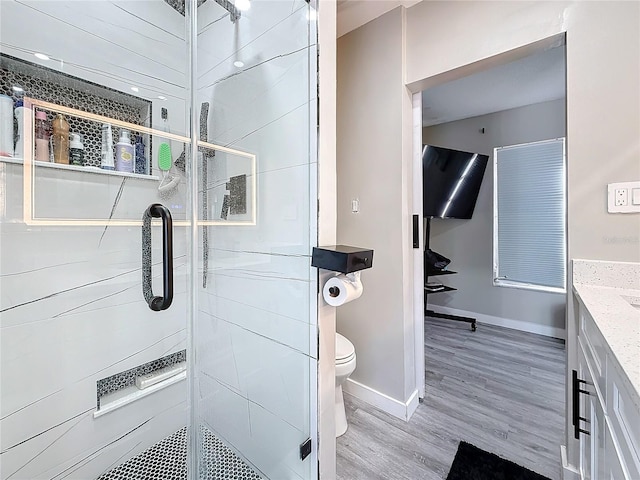 bathroom with toilet, vanity, a shower stall, wood finished floors, and baseboards