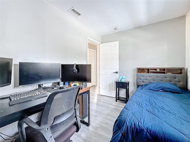 bedroom featuring light wood-type flooring, visible vents, and a textured ceiling