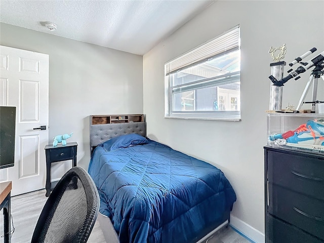 bedroom featuring baseboards, a textured ceiling, and wood finished floors