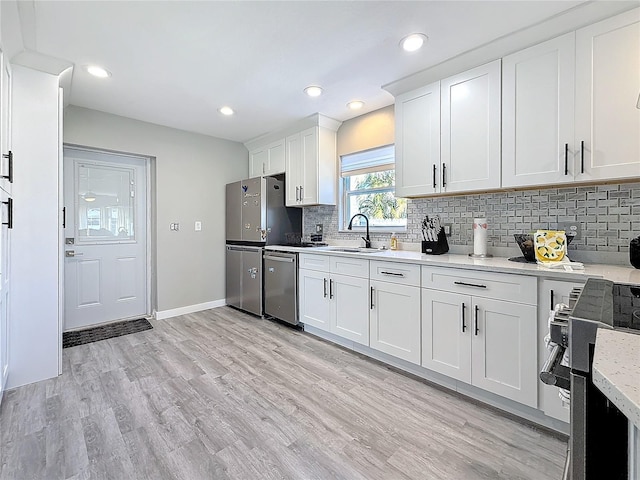 kitchen featuring white cabinets, decorative backsplash, appliances with stainless steel finishes, light wood-style floors, and a sink