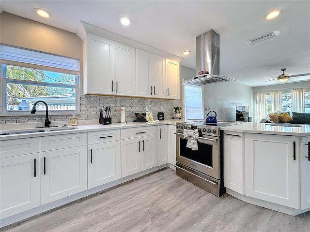 kitchen with visible vents, island range hood, high end range, light countertops, and a sink