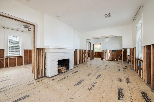 unfurnished living room featuring wainscoting, a brick fireplace, visible vents, and a ceiling fan