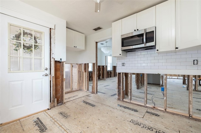 kitchen with visible vents, white cabinets, ceiling fan, stainless steel microwave, and backsplash