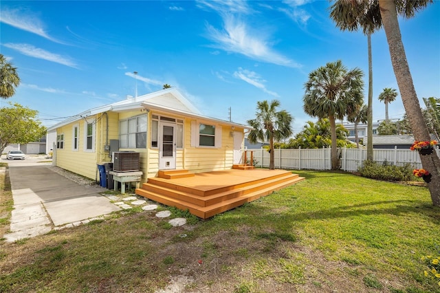 rear view of house featuring fence, a wooden deck, and a lawn