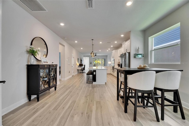 kitchen with a kitchen island with sink, white cabinetry, visible vents, and stainless steel fridge with ice dispenser