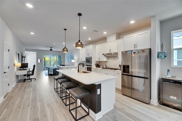 kitchen with a kitchen island with sink, white cabinetry, appliances with stainless steel finishes, backsplash, and light wood finished floors