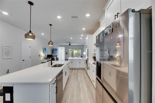 kitchen featuring visible vents, light wood-style flooring, appliances with stainless steel finishes, a kitchen island with sink, and a sink