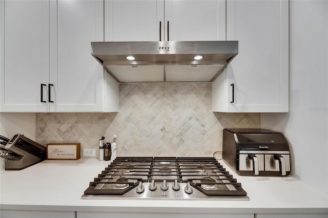 kitchen featuring under cabinet range hood, white cabinets, light countertops, tasteful backsplash, and stainless steel gas stovetop