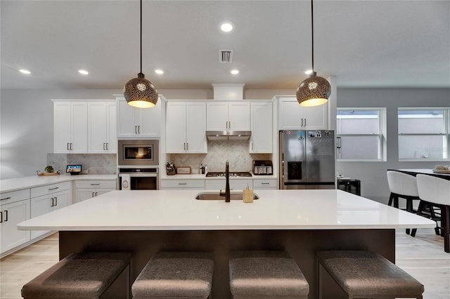 kitchen featuring a breakfast bar area, stainless steel appliances, tasteful backsplash, light wood-style flooring, and under cabinet range hood