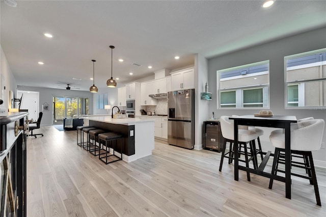 kitchen with a breakfast bar, stainless steel appliances, white cabinetry, a sink, and an island with sink