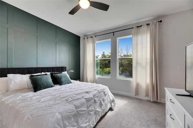 bedroom with light carpet, a decorative wall, a ceiling fan, and baseboards