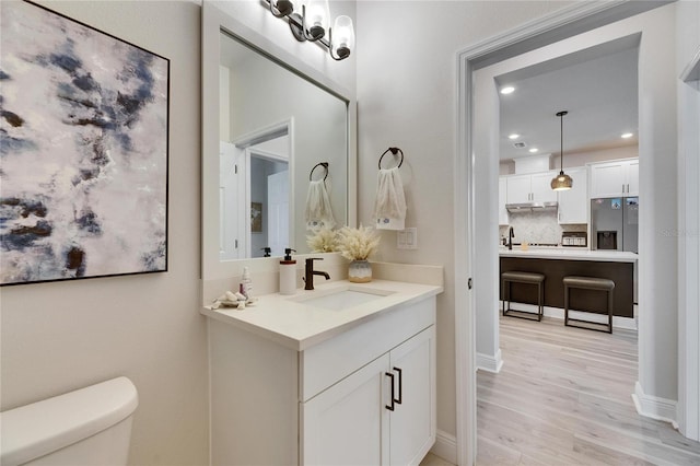 bathroom with toilet, decorative backsplash, wood finished floors, and vanity