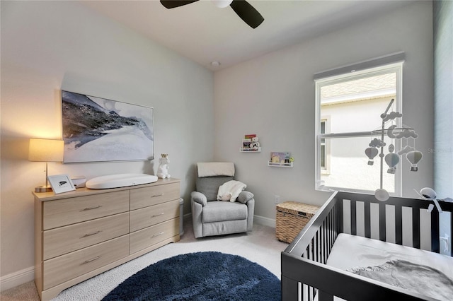 bedroom with a ceiling fan, light carpet, a crib, and baseboards