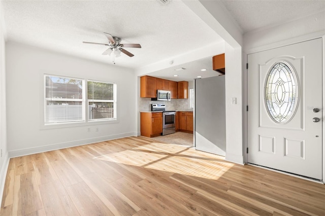 entryway featuring ceiling fan, light wood finished floors, a textured ceiling, and baseboards