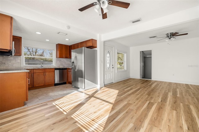 kitchen featuring appliances with stainless steel finishes, a wealth of natural light, brown cabinetry, and backsplash