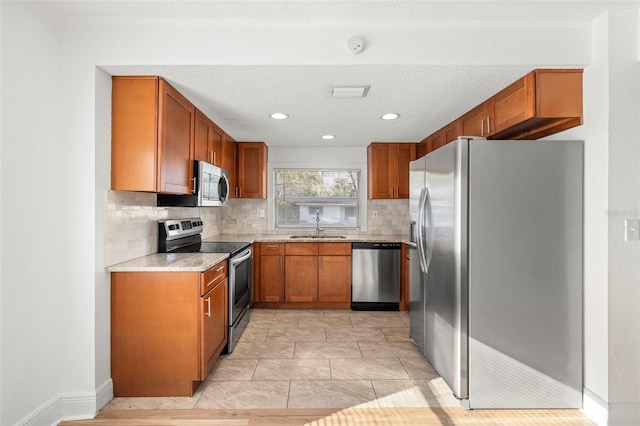 kitchen with brown cabinets, stainless steel appliances, decorative backsplash, a sink, and a textured ceiling